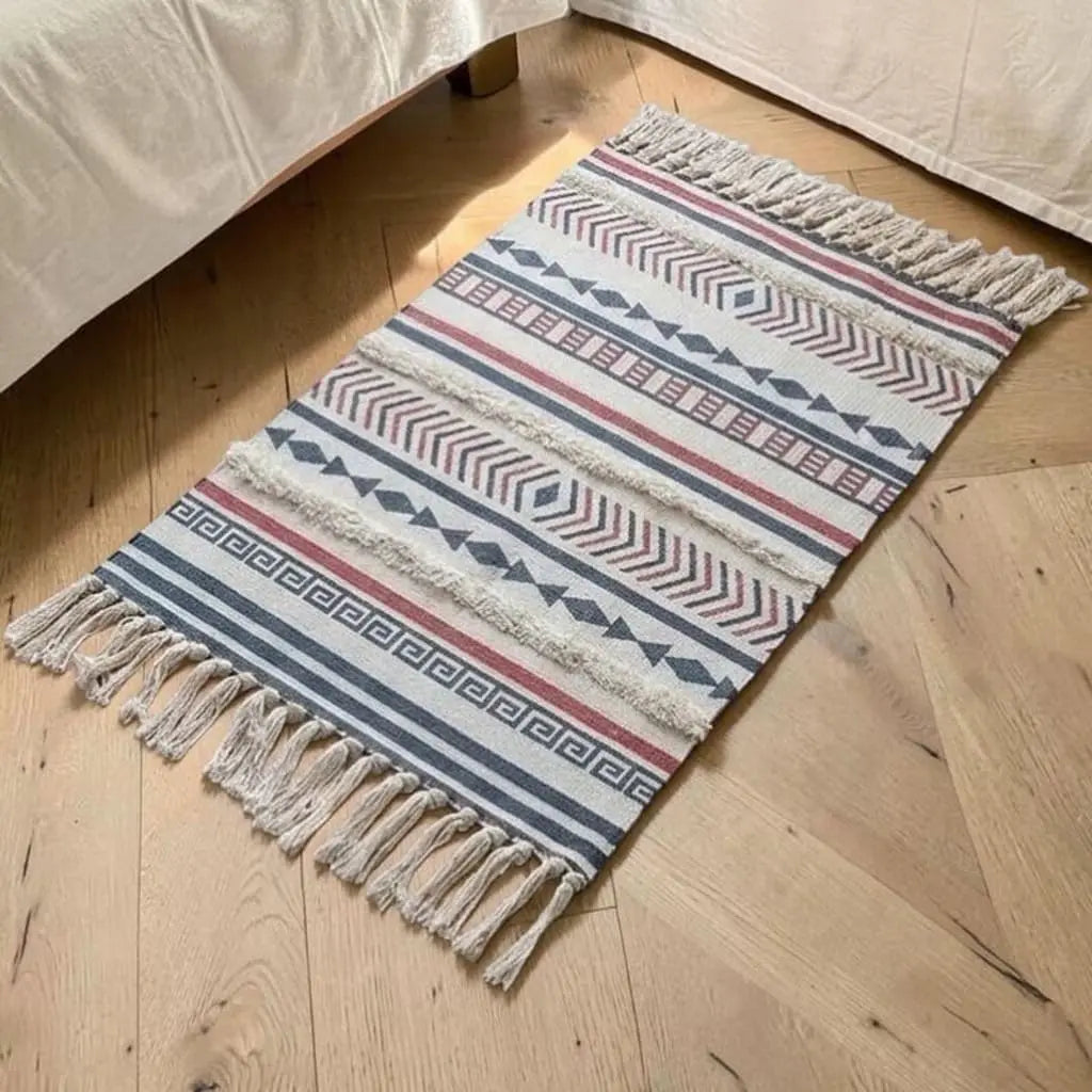 Tapis bohème AROHA placé au pied d’un lit sur un parquet en bois.