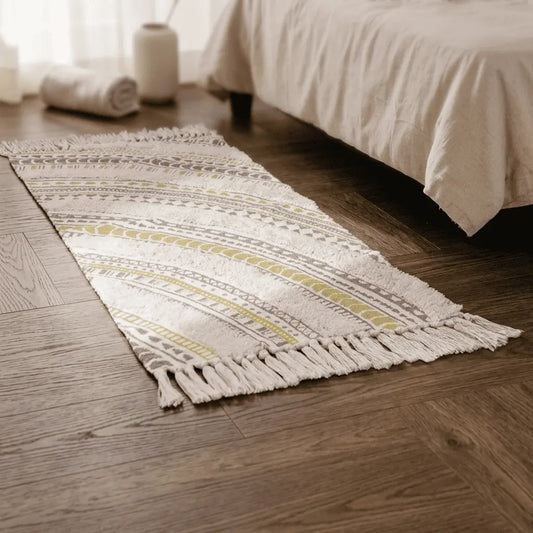 Tapis bohème SABLE écru à motifs rayés placé au pied d’un lit, sur un parquet foncé.