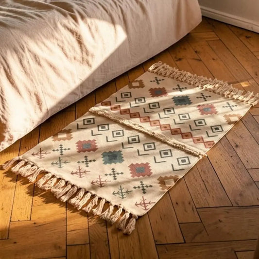 Tapis bohème beige à motifs géométriques colorés, placé au pied d’un lit sur un parquet en bois.