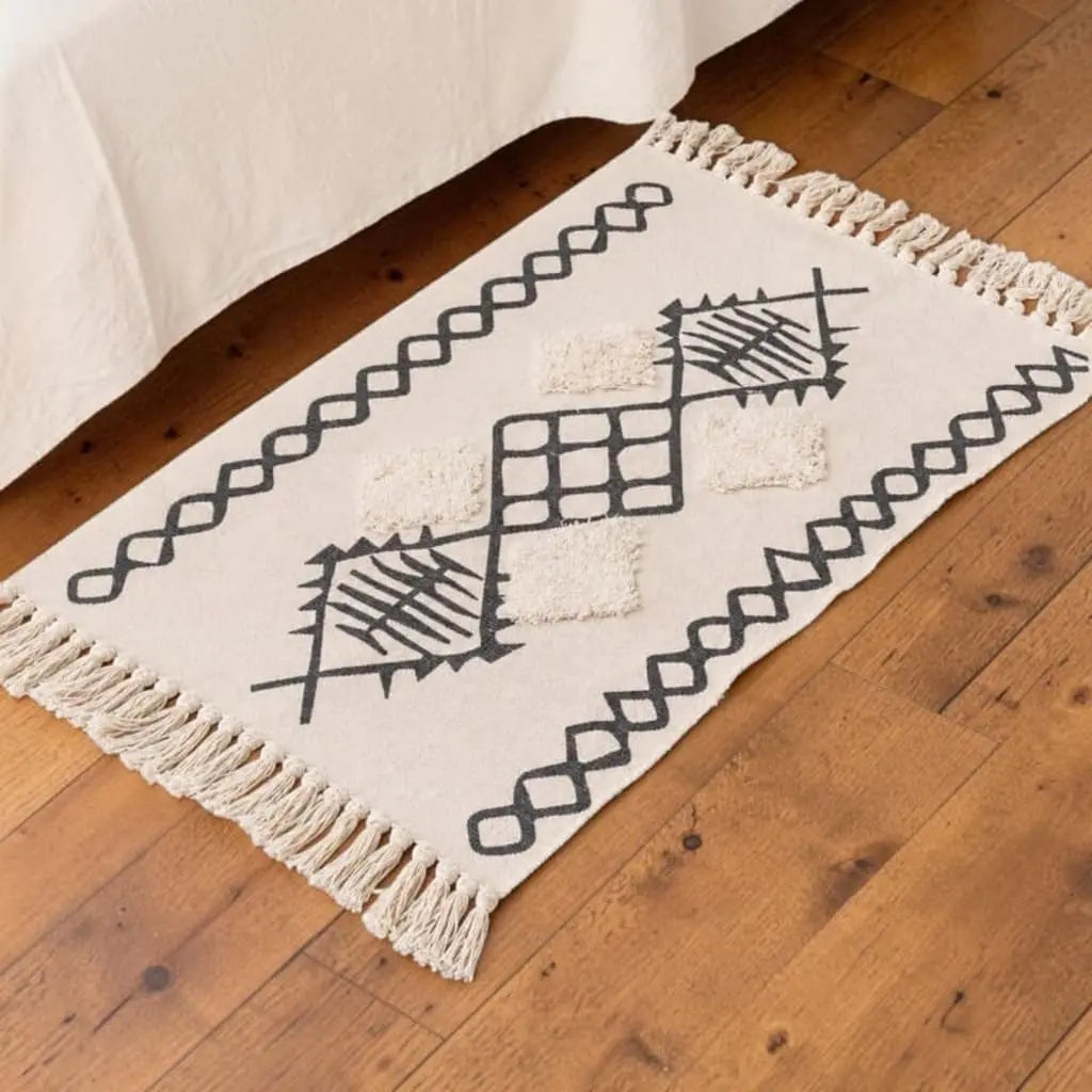 Tapis bohème AZRANE écru à motifs berbères noirs, installé dans une chambre sur un parquet en bois.