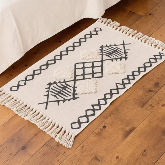 Tapis bohème AZRANE écru à motifs berbères noirs, installé dans une chambre sur un parquet en bois.