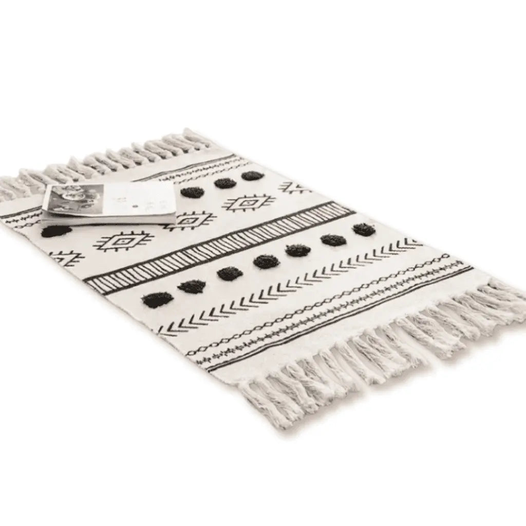 Tapis bohème écru à motifs ethniques noirs et franges décoratives.
