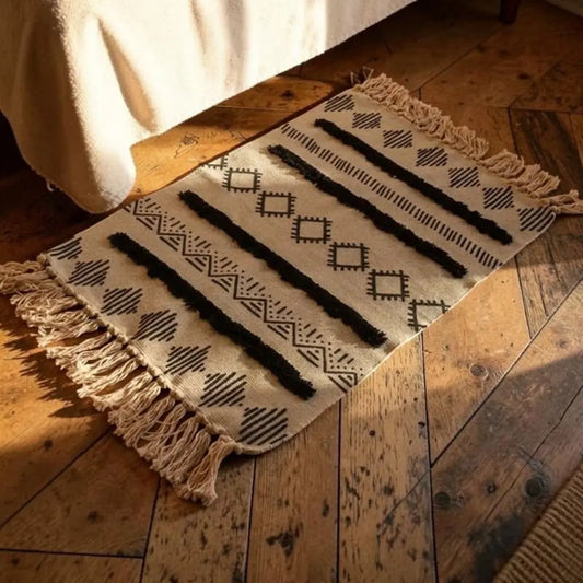 Tapis bohème AKSEL placé au pied d’un lit sur un parquet en bois.