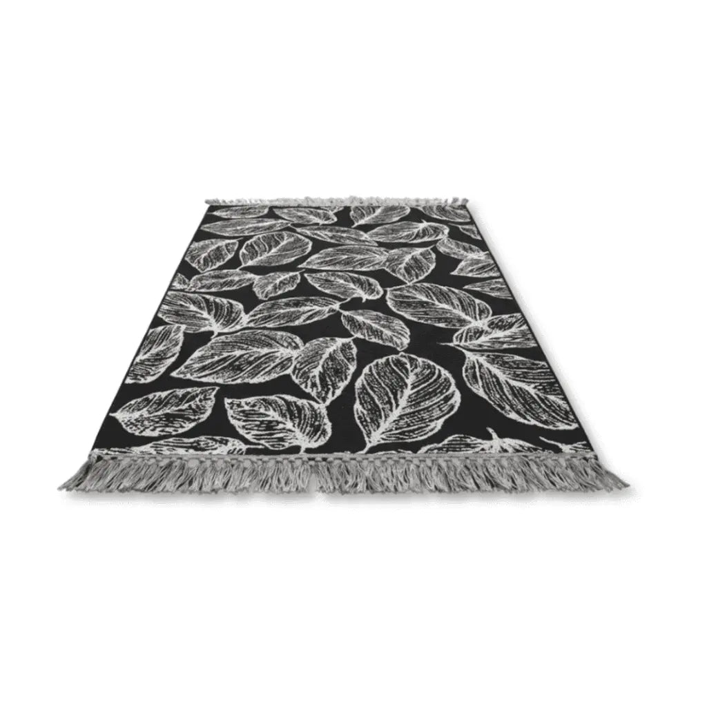 Tapis bohème noir à motifs de feuilles blanches et franges décoratives.