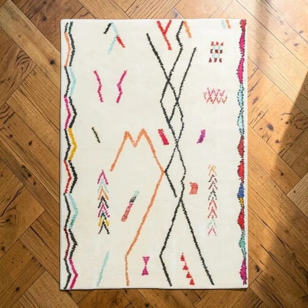 Tapis berbère aux motifs géométriques orange, noir, rose et turquoise, posé sur un parquet.