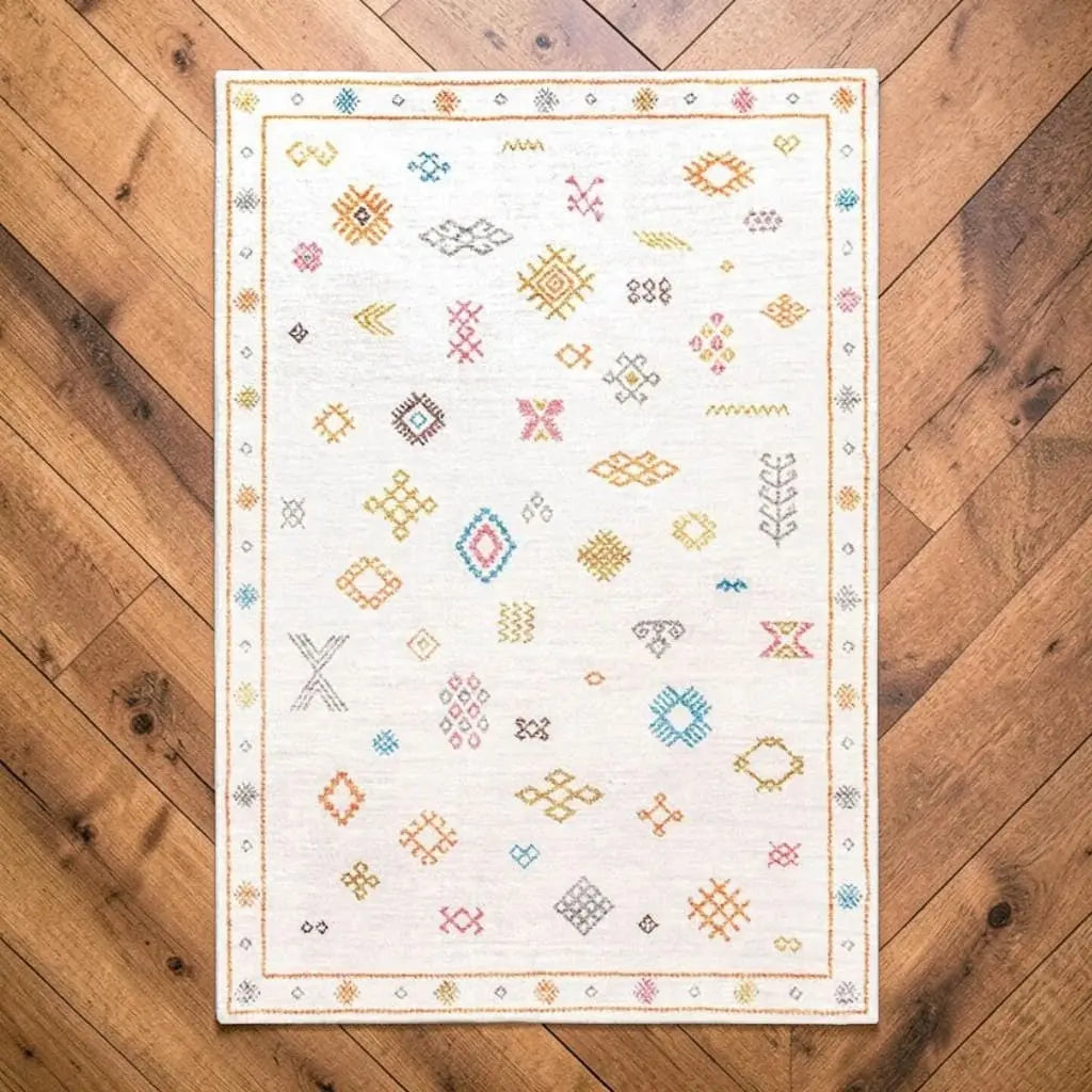 Tapis berbère écru et pastel posé sur un parquet en bois.